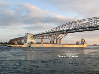 Samuel de Champlain and Innovation (Detroit) sweep under the Bluewater Bridges as the setting sun nears the horizon.